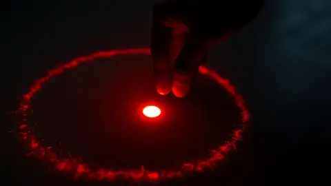 Hand drawing a glowing circle with a dot in the middle on a dark wooden floor