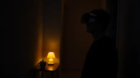 Lone player wearing a headset in a quiet apartment at night with a lamp and mug nearby