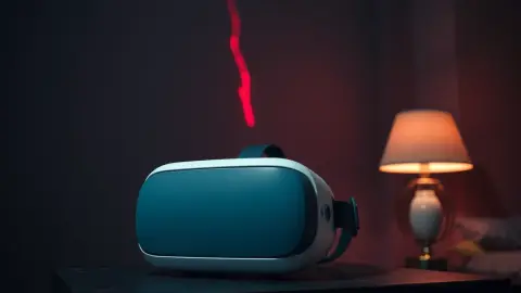 White VR headset on a desk in a dim bedroom with a faint red glow reflected on its visor