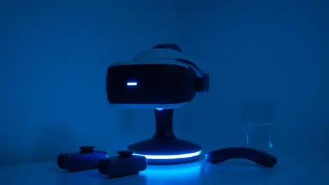 VR headset on a charging stand with controllers and a glass of water in a dim room