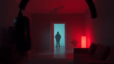 Dim living room in mixed reality with a cracked wall and a faint figure in the doorway