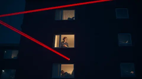 Apartment building at night with one window showing a player ducking under red lasers