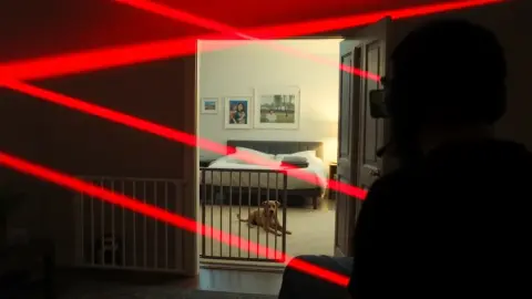 Living room with baby gate and sleeping dog while a player ducks under lasers