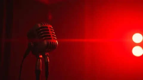Vintage studio microphone in a dim booth with a soft red glow and a faint laser beam behind it