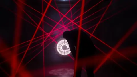 Dark room with a figure bending backwards under a web of red laser beams near a wall safe