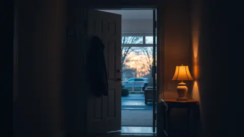 Hallway with a coat and warm lamp seen from an open front door at dusk