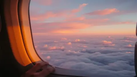 Calm hand resting on an airplane armrest with a sunrise sky in the window