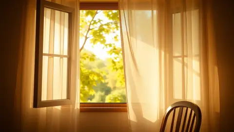 Sheer curtains moving at an open window with a sunlit garden outside