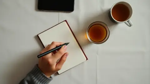 Hand writing a short note beside a phone and tea before a meditation