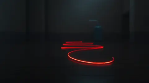 Thin glowing wire snaking across a wooden floor toward a small blue tank